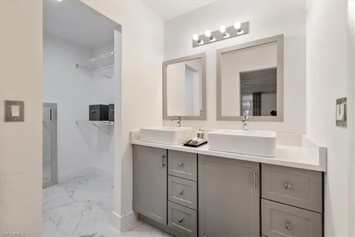 Bathroom featuring a walk in closet, double vanity, and light marble finish flooring