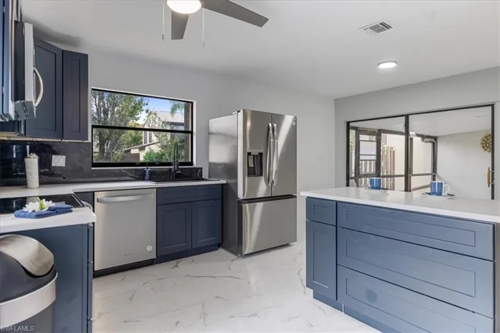 Kitchen with stainless steel appliances, blue cabinets, light marble finish flooring, light stone counters, and recessed lighting