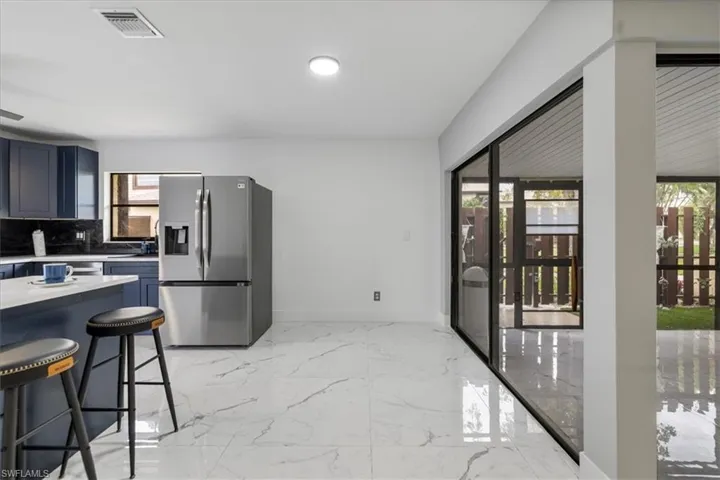 Kitchen featuring light countertops, light marble finish floors, stainless steel refrigerator with ice dispenser, blue cabinetry, and a kitchen breakfast bar