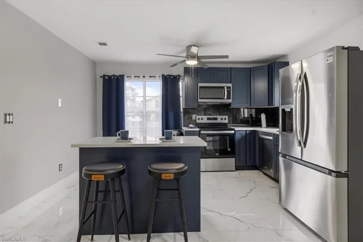 Kitchen with appliances with stainless steel finishes, a kitchen breakfast bar, light countertops, a center island, and light marble finish flooring