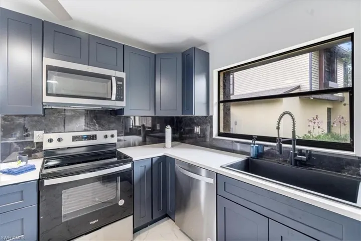Kitchen featuring appliances with stainless steel finishes, backsplash, light marble finish flooring, light stone counters, and gray cabinetry