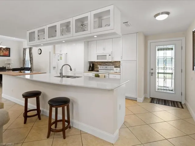 Open-concept kitchen featuring white cabinetry, a stone-look countertop, stainless steel appliances, a tile backsplash, and tile flooring