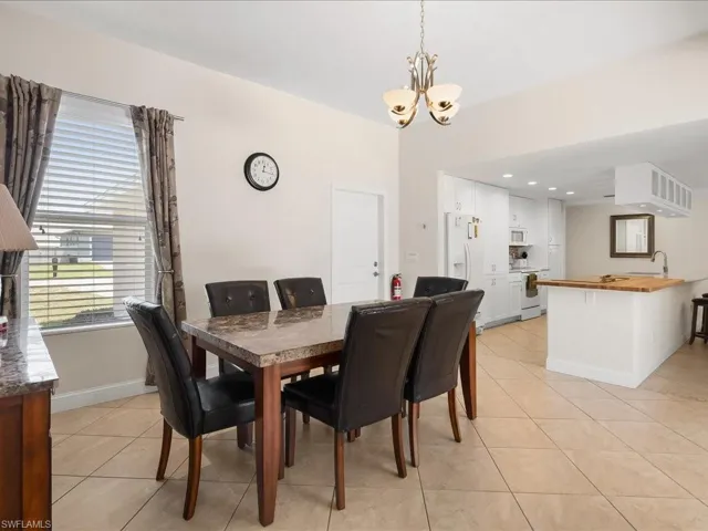 Open concept dining area featuring a chandelier, tile flooring, and a kitchen with white cabinetry and a wood-finish island countertop