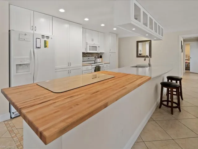 Kitchen featuring a large central island with a wood-finish countertop and a separate white countertop with an undermount sink