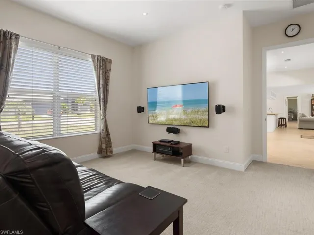 Carpeted interior space featuring a large window with blinds, recessed lighting, and a wide entryway to another room with wood-finish flooring
