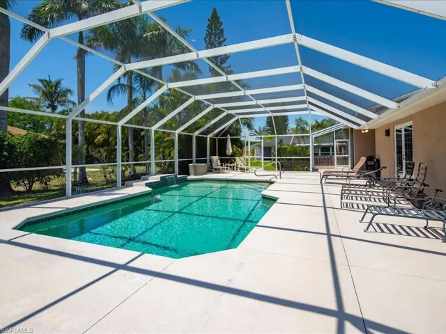 Screened outdoor pool area featuring a rectangular pool with integrated steps, a surrounding paved deck, and a stucco exterior wall