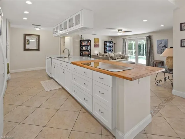 Central kitchen island with white shaker cabinetry, an integrated sink, and a contrasting wood-finish countertop