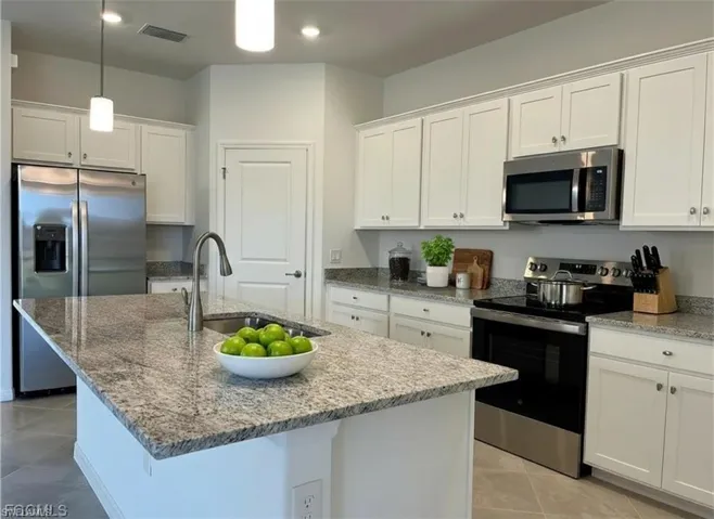 Kitchen with stainless steel appliances, white cabinets, light stone countertops, and a center island with sink