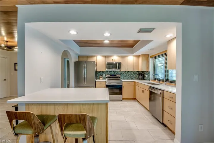 Kitchen with a raised ceiling, light tile patterned floors, light brown cabinetry, a breakfast bar, and appliances with stainless steel finishes