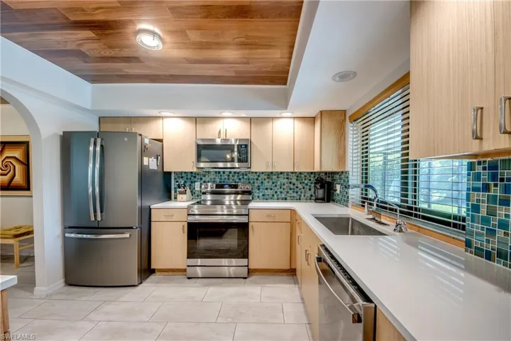 Kitchen featuring light brown cabinetry, light tile patterned floors, appliances with stainless steel finishes, tasteful backsplash, and sink