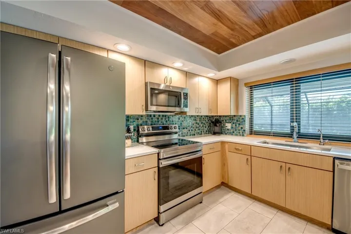 Kitchen featuring light tile patterned floors, sink, decorative backsplash, appliances with stainless steel finishes, and light brown cabinets