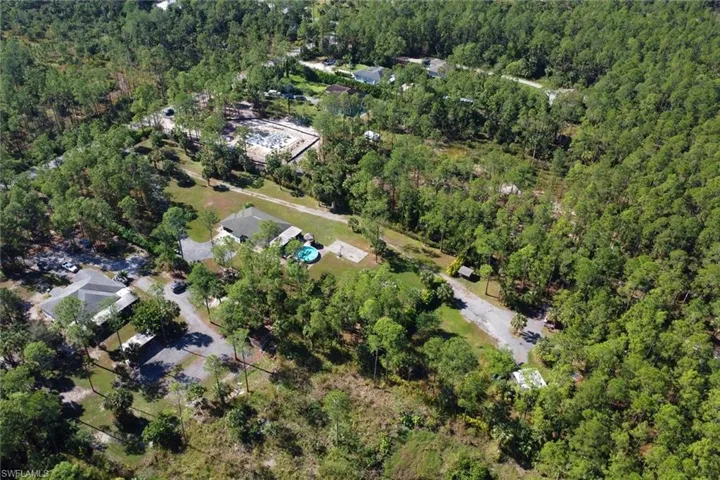 View of the exterior of the lot. You can see the paved driveway that leads you to the 2 car garage and a large cleared area in the back with a canopy and shipping container with extended roof.