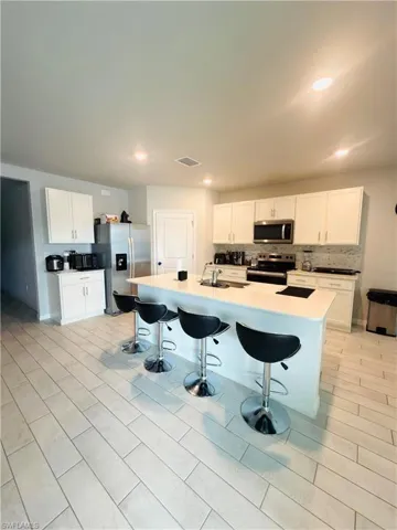Kitchen with white cabinets, a kitchen bar, stainless steel appliances, an island with sink, and tasteful backsplash