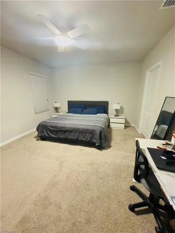 Bedroom with light colored carpet, a ceiling fan, and an office area