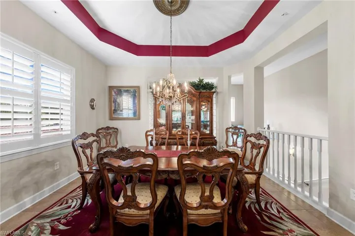 Tray ceiling with contrasting accent, plantation shutters, tiled flooring, and a decorative chandelier