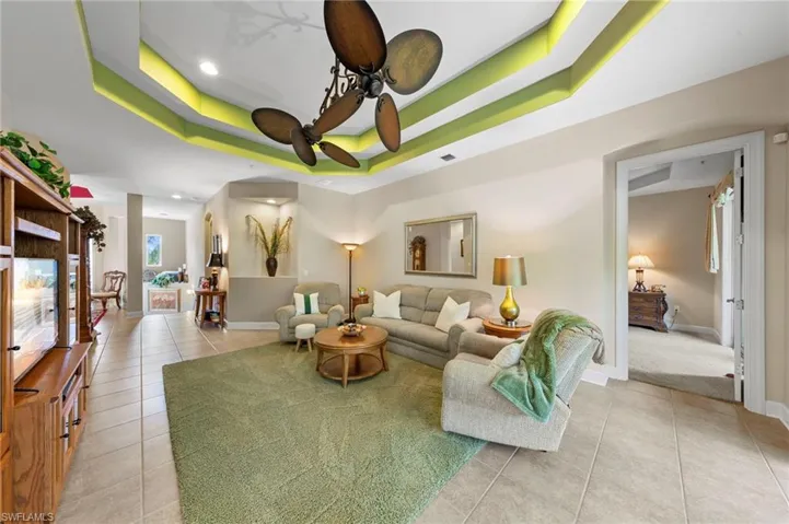 Tray ceiling with integrated lighting, tiled flooring, built-in display cabinetry, ceiling fan