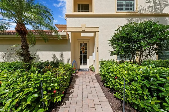 Paver walkway framed by mature landscaping, leading to a front entry with a glass-paneled door