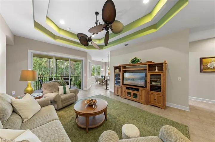 Coffered ceiling with integrated lighting, multiple ceiling fans, sliding glass door, tiled flooring, and a built-in entertainment center