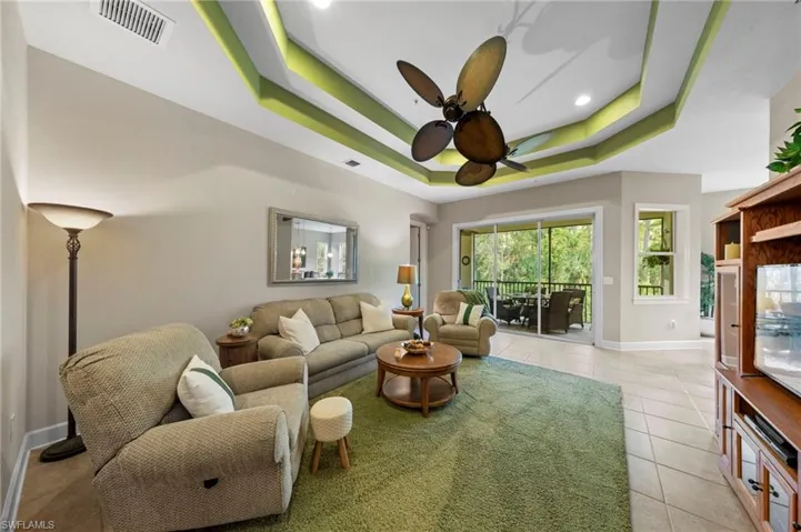 Tray ceiling with accent lighting, ceiling fan, ceramic tile flooring, and sliding glass doors to a screened outdoor area