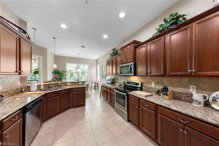 Kitchen featuring wood cabinetry, stone countertops, stainless steel appliances, a tile backsplash, and recessed lighting