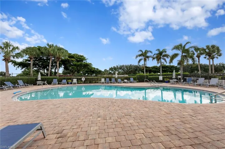 Resort-style pool area featuring a large curvilinear pool, extensive paver decking, and surrounding mature palm trees