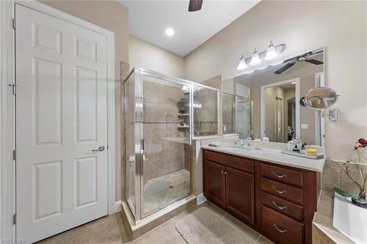 Bathroom featuring a glass-enclosed shower with tile surround, a built-in vanity with rich wood-finish cabinetry, a single sink, and a large wall-mounted mirror