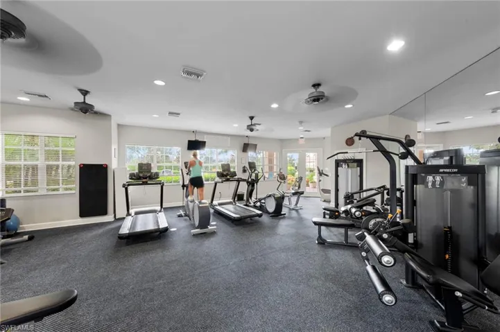 Fitness center featuring cardio equipment, strength training machines, mirrored walls, ceiling fans, and multiple windows