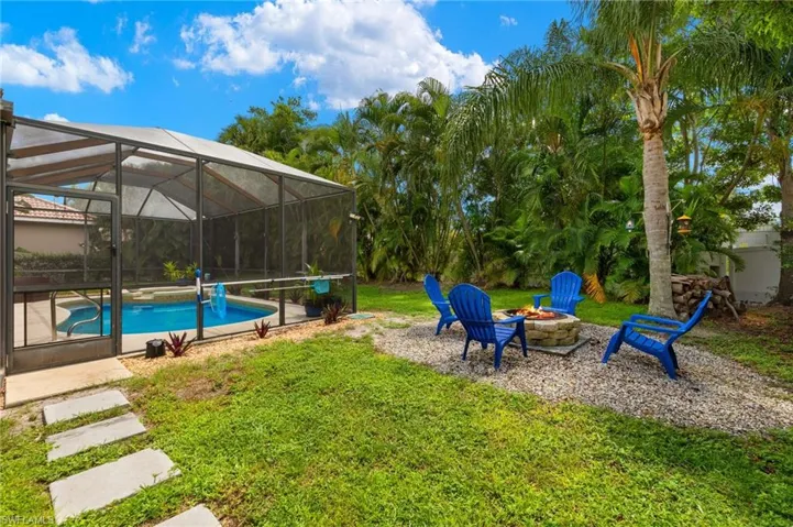 View of green lawn featuring an outdoor fire pit, glass enclosure, an outdoor pool, a patio area, and a sunroom