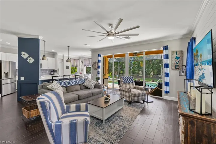 Living room featuring crown molding, a ceiling fan, dark wood-type flooring, and a sunroom