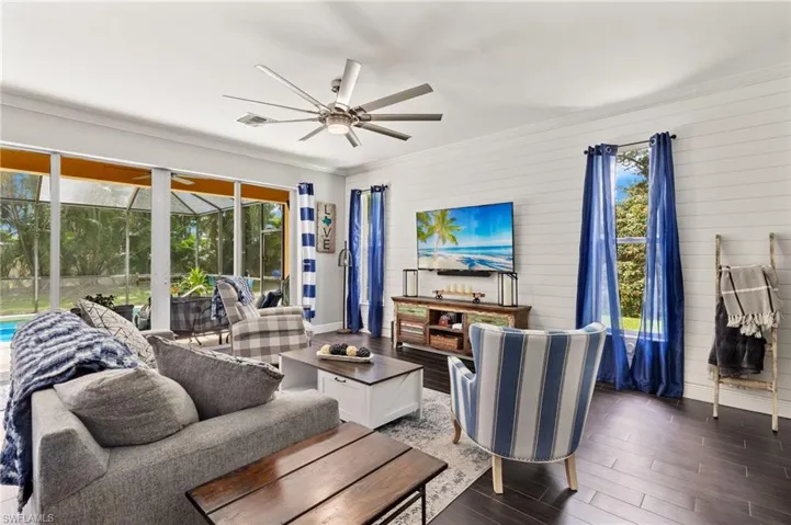 Living area featuring a sunroom, wood finished floors, ornamental molding, a ceiling fan, and wood walls