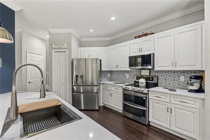Kitchen with stainless steel appliances, white cabinetry, crown molding, light stone counters, and recessed lighting