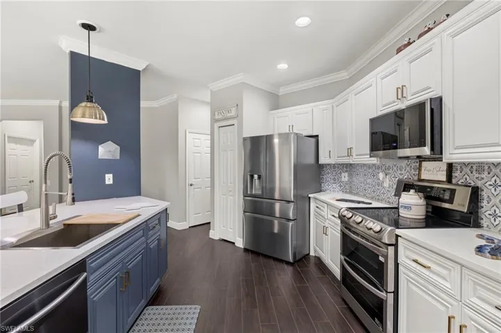 Two tone kitchen with stainless steel appliances, light stone countertops, dual tone cabinetry, ornamental molding, and dark wood-style flooring