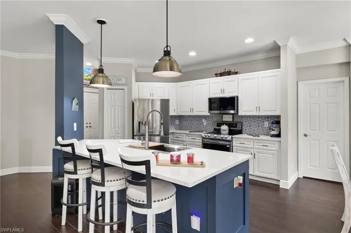 Dual tone kitchen featuring stainless steel appliances, decorative light fixtures, a breakfast bar area, dark wood finished floors, and tasteful backsplash