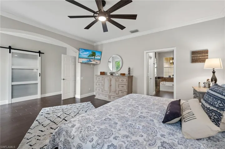Bedroom featuring a barn door, ensuite bathroom, crown molding, dark wood finished floors, and ceiling fan