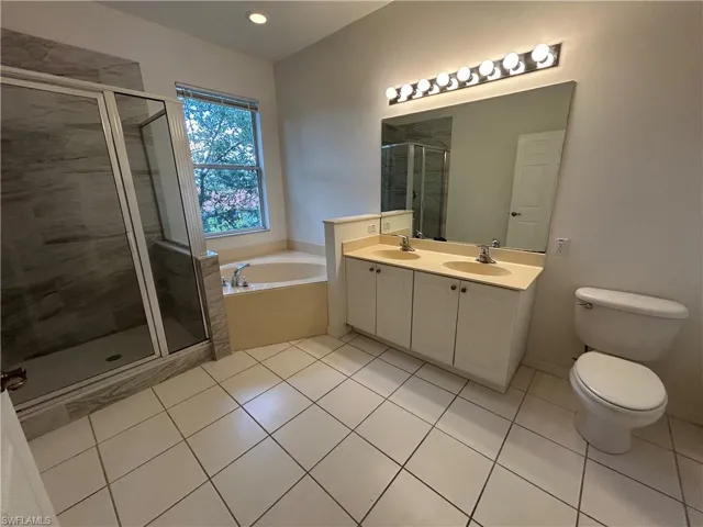 Full bath featuring light tile patterned floors, a bath, a shower stall, and double vanity