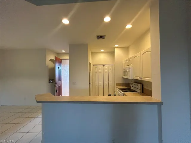 Kitchen with white appliances, recessed lighting, white cabinetry, light countertops, and a peninsula