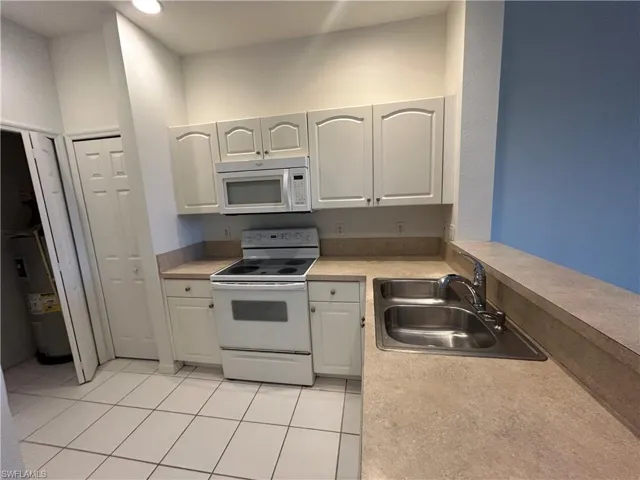 Kitchen featuring white appliances, light tile patterned flooring, light countertops, electric water heater, and white cabinets