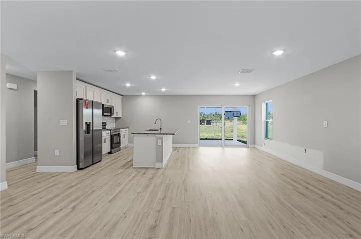 Kitchen with appliances with stainless steel finishes, white cabinetry, and island with sink