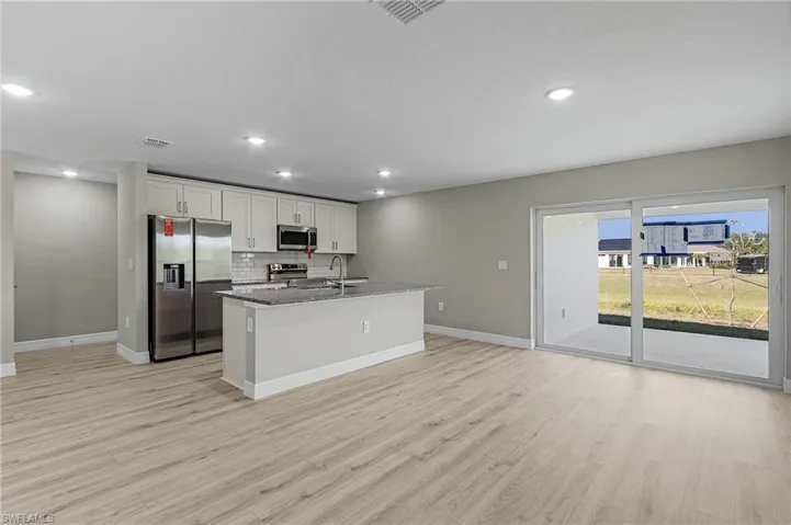 Kitchen with tasteful backsplash, white cabinetry, stainless steel appliances, and granite counters.