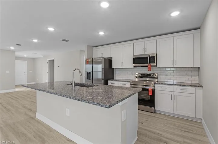 Kitchen with tasteful backsplash, white cabinetry, stainless steel appliances, and granite counters.