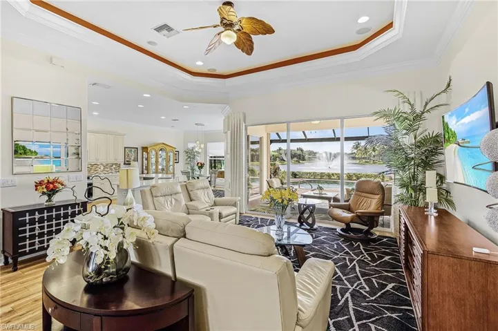 Tray ceiling with recessed lighting and crown molding, multi-panel sliding glass doors, and wood-finish flooring