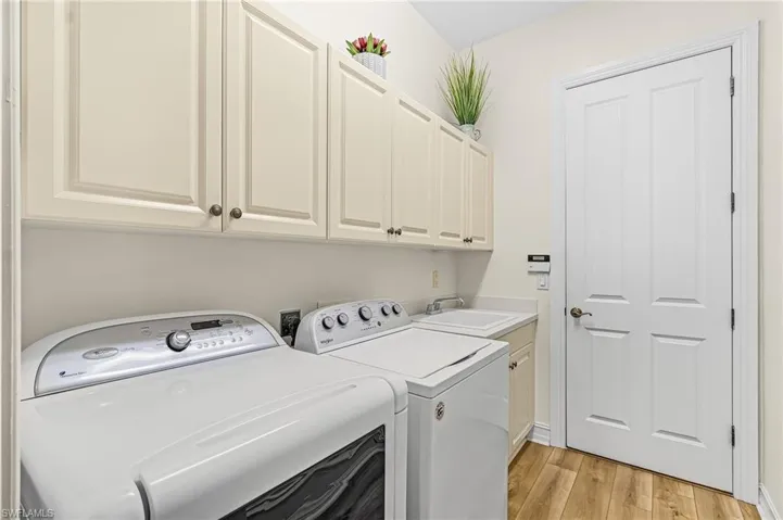 Laundry area featuring shaker-style upper cabinetry, wood-finish flooring, a built-in utility sink with a stone countertop, and a four-panel interior door