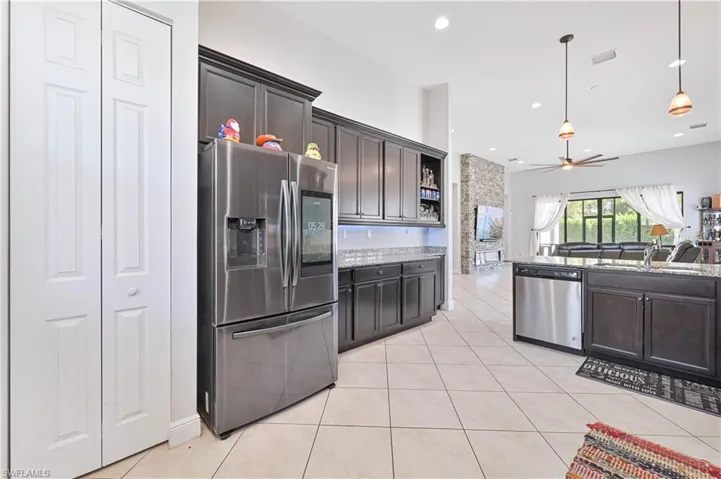 Kitchen with stainless steel appliances, dark wood finish cabinets, light stone countertops, and light tile patterned flooring