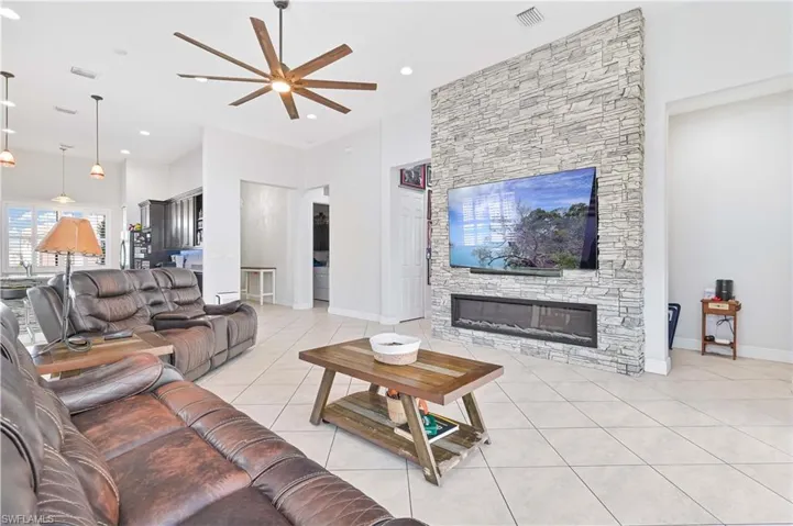 Living room with light tile patterned flooring, ceiling fan, a high ceiling, and a fireplace