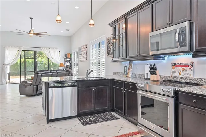 Kitchen featuring stainless steel appliances, light stone countertops, open floor plan, glass insert cabinets, and light tile patterned floors