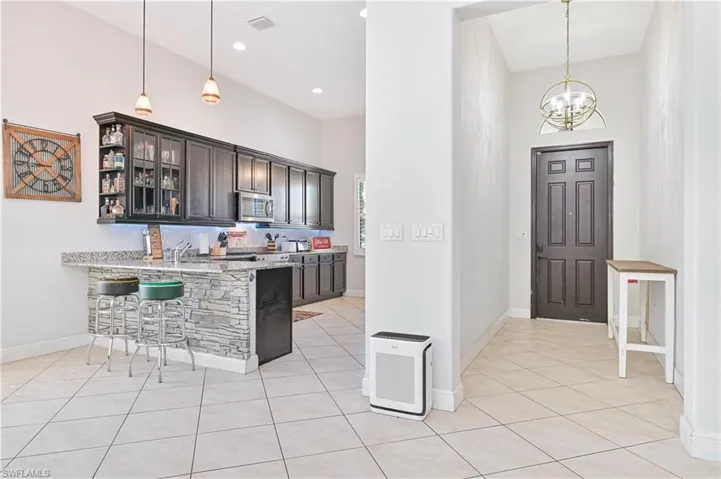 Kitchen with glass fronted cabinets, a kitchen breakfast bar, light stone countertops, light tile patterned floors, and a high ceiling