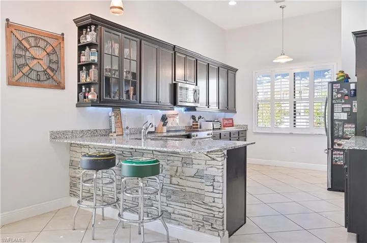 Kitchen with light stone counters, glass insert cabinets, light tile patterned floors, a kitchen bar, and stainless steel appliances