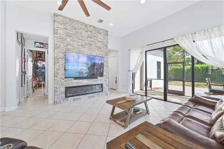Living area featuring light tile patterned floors, ceiling fan, a fireplace, and a high ceiling
