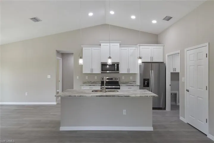 Kitchen featuring appliances with stainless steel finishes, white cabinets, an island with sink, and hardwood / wood-style floors