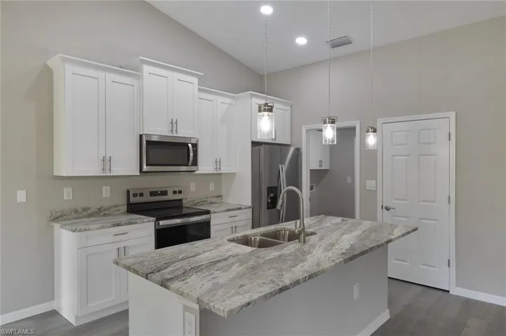 Kitchen featuring stainless steel appliances, white cabinets, a center island with sink, and sink